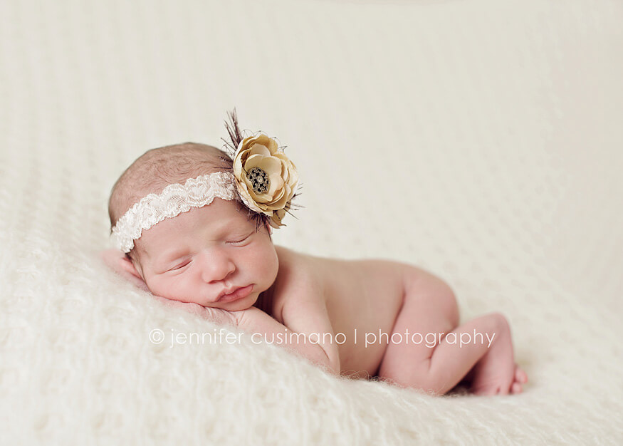 newborn baby girl on a white blanket with a flower vintage hair bow