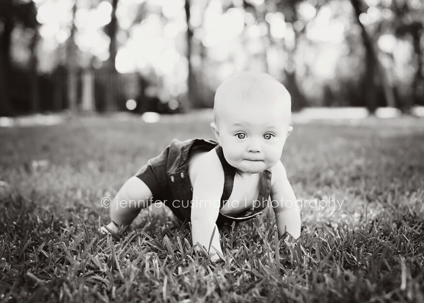black and white image of a baby boy trying to crawl in the grass