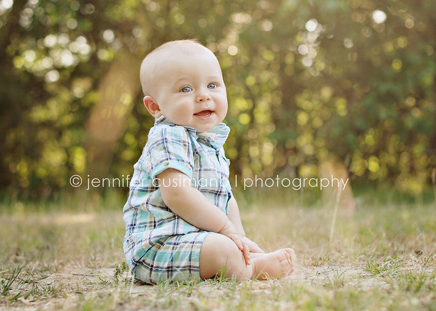 baby boy in plaid outfit sitting in the grass with sun flare