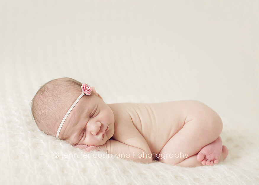 newborn baby laying on a white blanket with a pink hair bow