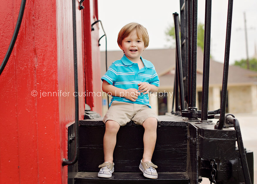 Two year old boy sitting on red train cart in Katy, TX
