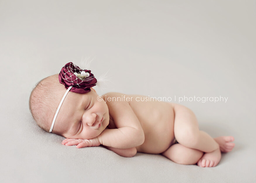 newborn baby sleepying on a gray blanket with a purple vintage hair bow