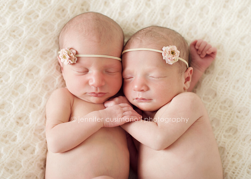 newborn girl twins with pink hair bows holding hands